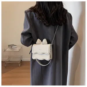 Detail of cream mini crossbody bag with wavy edge and decorative bow on grey blazer