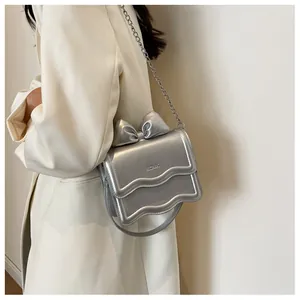 Detail of silver metallic handbag with bow accent and chain strap worn on white coat