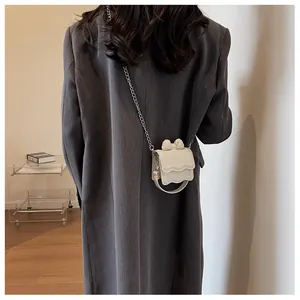 Chic beige mini square bag with bow detail and chain strap worn over a grey coat