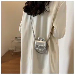 Detail of silver metallic mini bag with bow accent and scalloped edges on chain strap