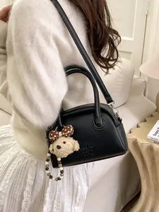 Minimalist black lychee leather baguette bag with plush bear charm and shoulder strap