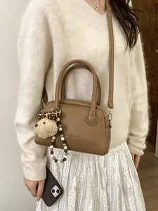 Minimalist brown pebbled leather Boston bag with plush bear charm and crossbody strap