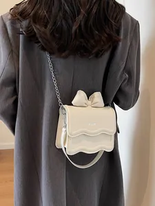 Chic beige crossbody bag with large bow detail and metal chain strap worn by model