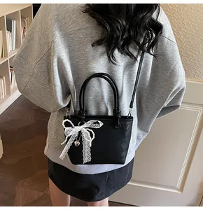 Dettaglio mini tote bag nera con fiocco in pizzo bianco, perle e ciondolo a cuore
