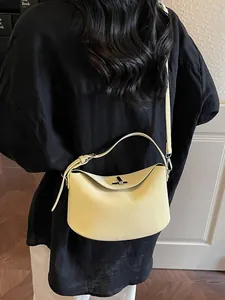 Minimalist cream yellow leather hobo bag with silver buckle worn as a crossbody