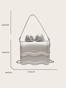 Silver metallic crossbody bag with a large 3D bow and KCMK logo, 17cm wide size guide