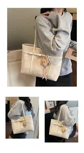 Detalle de bolso tote beige con correa de hebilla metálica y colgante de oso de peluche