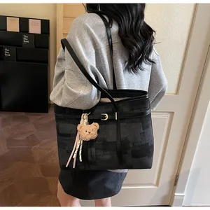 Detalle de bolso tote grande de lona negra con estampado geométrico y correa de cuero fina