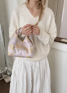 Gros plan d'un sac à main lilas aux motifs floraux porté avec une jupe plissée blanche