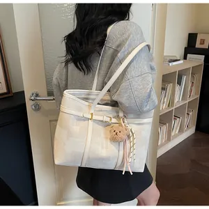 Detalle del bolso tote blanco crema con textura geométrica y un colgante de oso de peluche