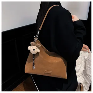 Nahaufnahme der braunen Wildleder-Tragetasche mit Teddybär-Anhänger und Metall-Namensschild