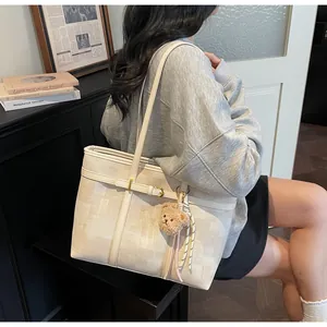 Detalle del bolso tote a cuadros con correa de cuero y amuleto de osito de peluche suave