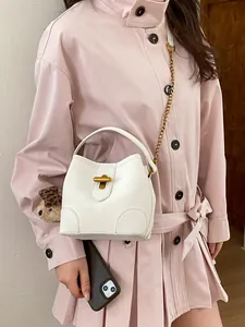 Elegante borsa a secchiello bianca con chiusura dorata e ciondolo a orso su modella