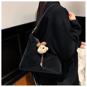 Detail der schwarzen Leder-Dreieckstasche mit einem süßen Teddybär-Plüsch-Anhänger