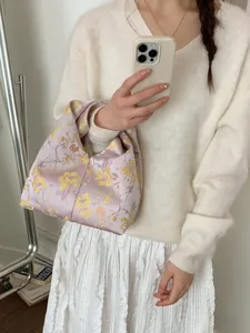 Sac seau minimaliste en jacquard violet avec motifs floraux dorés porté par un mannequin