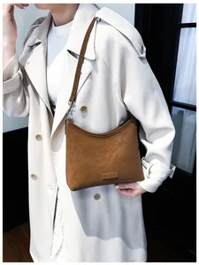Nahaufnahme einer großen dunkelbraunen Ledertasche mit Logo auf beige Trenchcoat