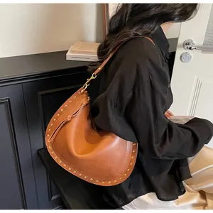 Close-up of brown leather hobo bag featuring decorative gold rivets and shoulder strap