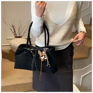 Détail d'un sac cabas en daim noir mat avec breloque léopard et glands sur la bandoulière