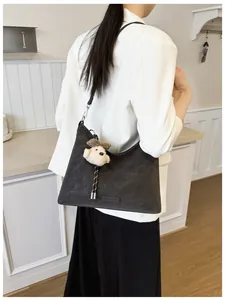 Detail der dunkelgrauen Wildleder-Einkaufstasche mit Bärenanhänger zum weißen Blazer