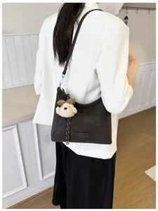 Detail der braunen Vintage-Tasche mit Plüschbär-Anhänger über einem weißen Blazer