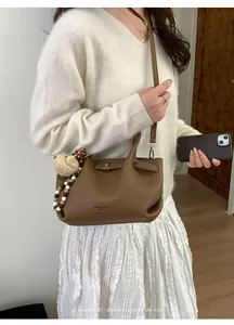 Brown lychee grain leather bucket bag with bear pendant and beaded strap details
