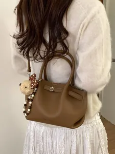 Borsa a secchiello minimalista in pelle marrone con orsetto di peluche e tracolla