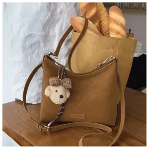 Detail einer braunen Wildleder-Tote-Bag mit einem süßen Teddybär-Anhänger auf Holztisch