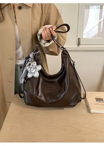 Detail der dunkelbraunen Hobo-Tasche aus Kunstleder mit verstellbarem Riemen und Blumenanhänger