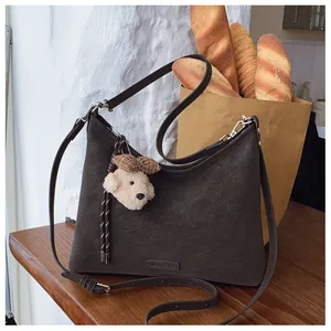 Details der braunen Vintage-Tasche mit Bärenanhänger auf rustikalem Holztisch