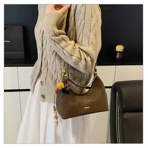 Detail of dark brown suede half-moon underarm bag with decorative plush ball charm