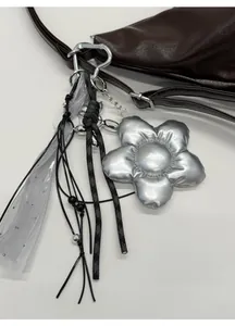 Detail eines silbernen Blumenanhängers aus Metall mit grauem Tüllband an einer Tasche