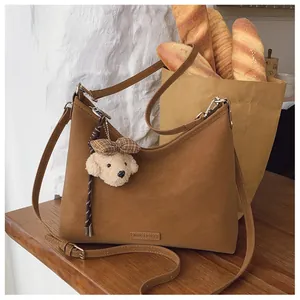 Detailaufnahme der braunen Wildledertasche mit süßem Welpen-Plüschanhänger und Logo-Prägung