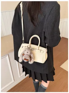 Detail der cremefarbenen Ledertasche mit silbernen Beschlägen und Plüschhasen am Modell