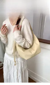 Shoulder bag detail view showing cream leather texture and drawstring ribbon charm decoration