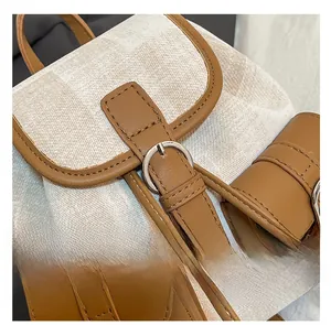Detail of stylish backpack featuring textured beige fabric and brown leather strap buckle