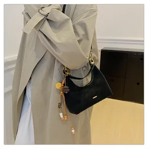 Detail of black suede hobo bag with vintage tassel charm worn with a khaki coat