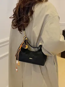 Minimalist black crescent shoulder bag with tassel charm styled on a beige trench coat