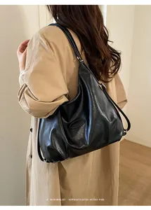 Detail einer großen schwarzen Leder-Hobo-Tasche mit Logo, getragen auf einem beigen Mantel