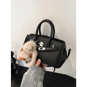 Klassische schwarze Lederhandtasche mit Metalldrehverschluss und süßem Hasen-Anhänger