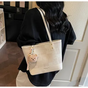 Close-up of beige tote bag with leather trim, teddy bear charm, and elegant gold lettering