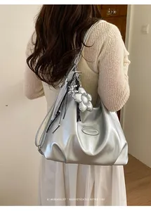Silberne Tragetasche mit Blumenanhänger und Metallic-Finish, getragen als Umhängetasche