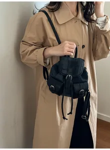 Detail of mini versatile backpack in grey denim and black leather on beige trench coat