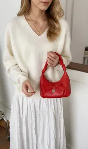 Detail of red pleated handle handbag featuring a decorative bow and silver heart pendant