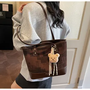 Detail of a brown jacquard tote bag with leather trim and a cute plush bear charm