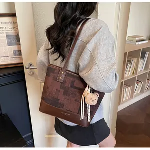 Detail view of contrast stitch tote bag featuring checkered pattern and plush bear charm