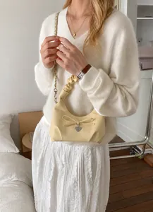 Detail showing cream pleated shoulder bag with bow decor and silver heart pendant