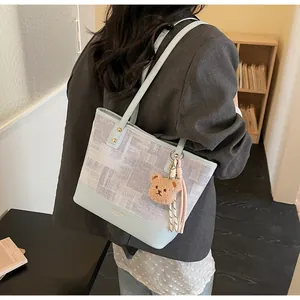 Detail view of light blue and gray patchwork tote bag with luxury lettering and bear charm