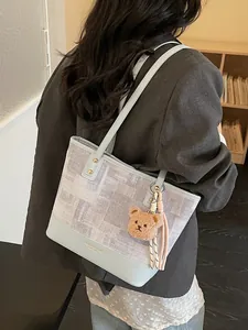 Blue and gray textured tote bag with bear charm shown on model in a modern office