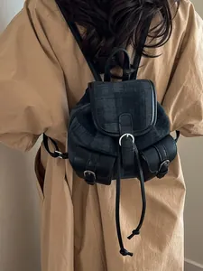 Woman wearing a vintage washed denim mini backpack with leather trim over a beige coat