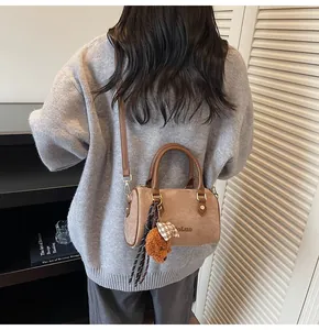 Brown suede Boston bag with teddy bear charm shown worn as a stylish crossbody bag